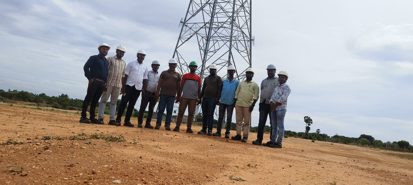 Client team in hard hats after Eduforce training at a wind and power site, with a transmission tower behind them