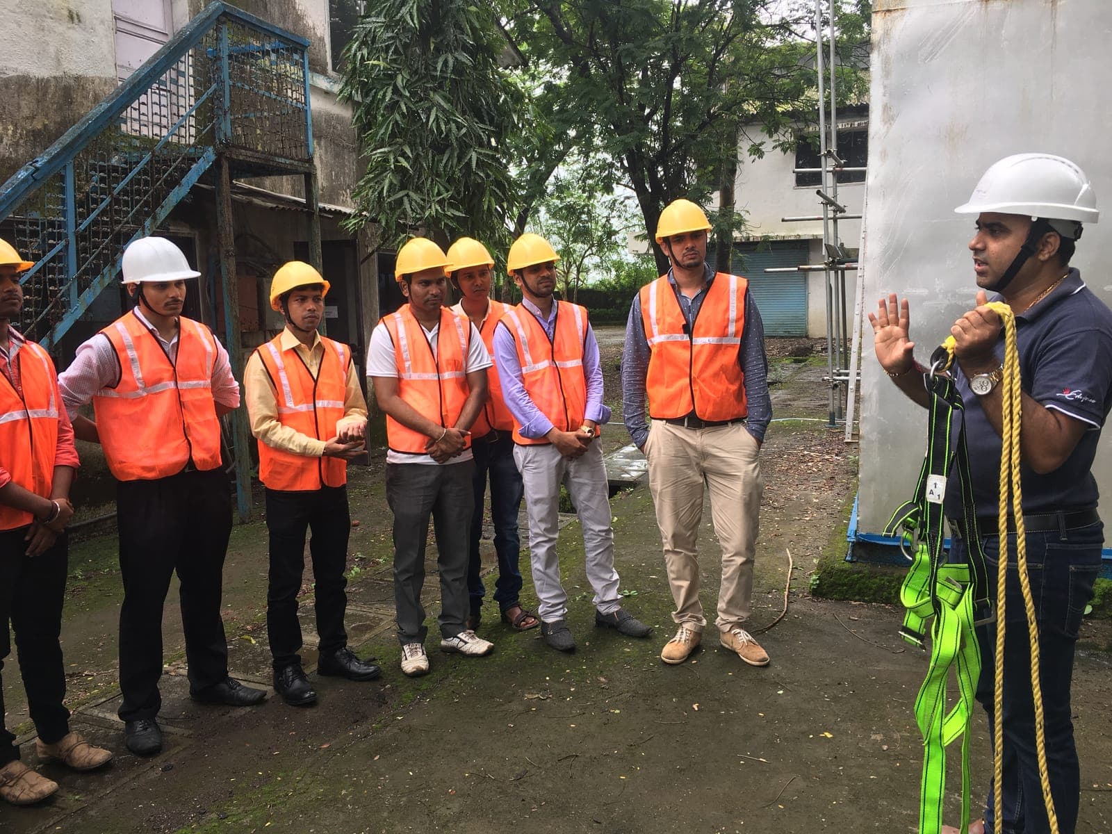 Eduforce trainer explaining a full-body harness and lanyard to trainees in hard hats and high-visibility vests at the training centre