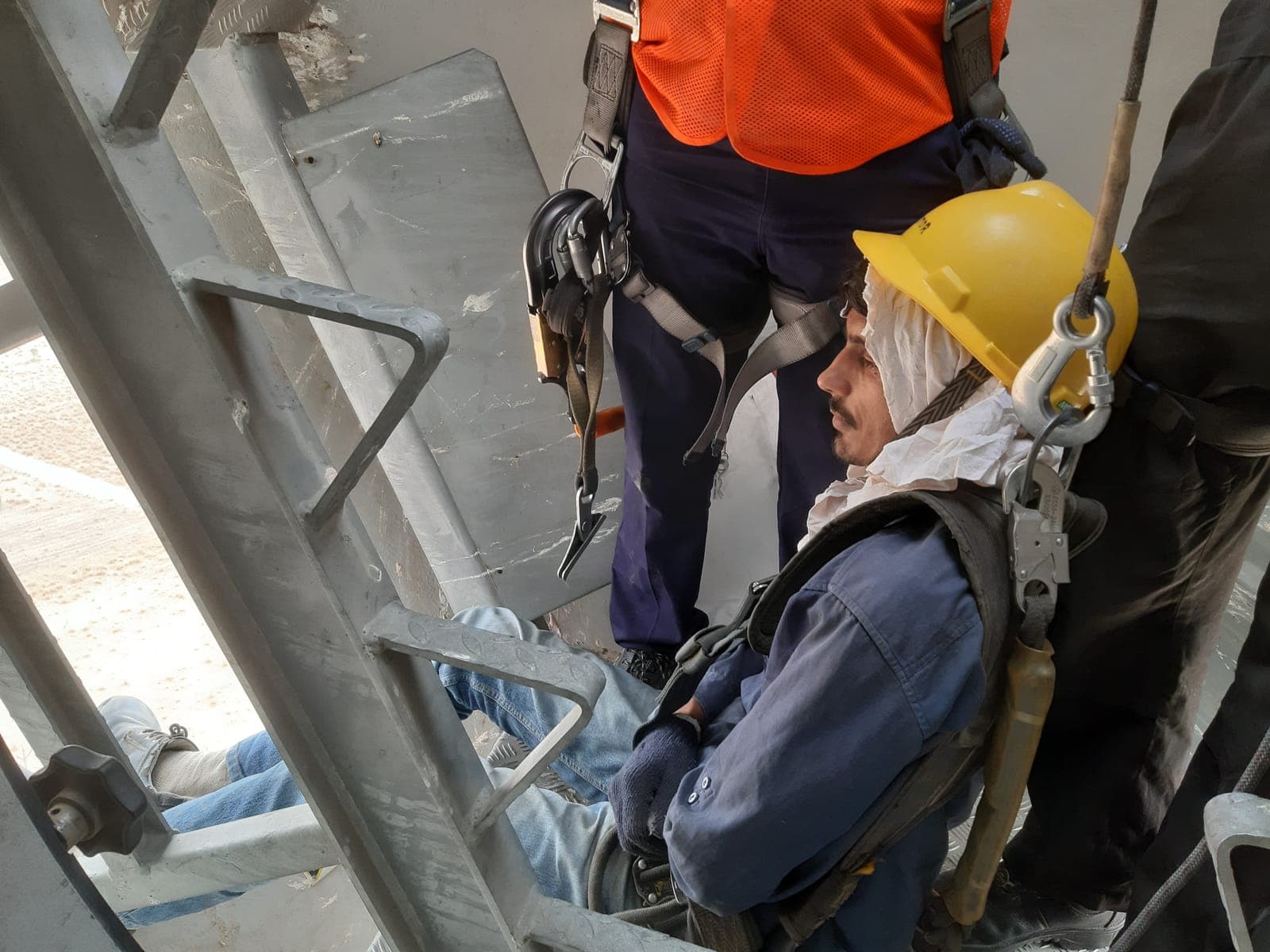 Rescue practice inside a wind turbine tower: a technician in helmet and harness secured to the rescue line beside the ladder
