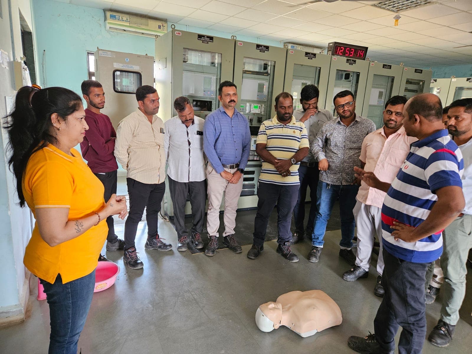 Eduforce trainer speaking to employees standing in a control room, with a CPR manikin on the floor in front of them