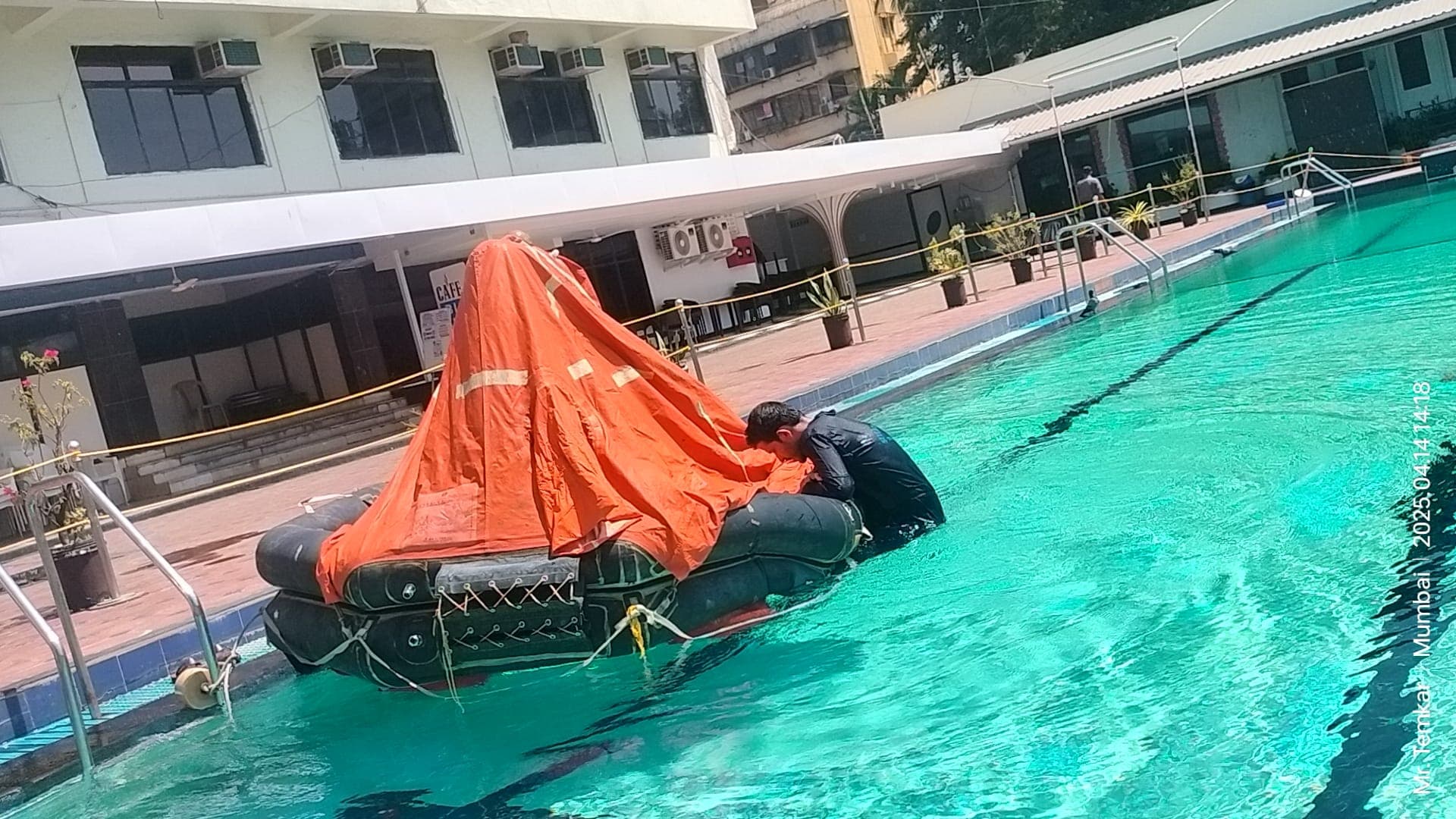 Participant working at the entrance of an inflated liferaft with its canopy erected in a training pool during sea survival training