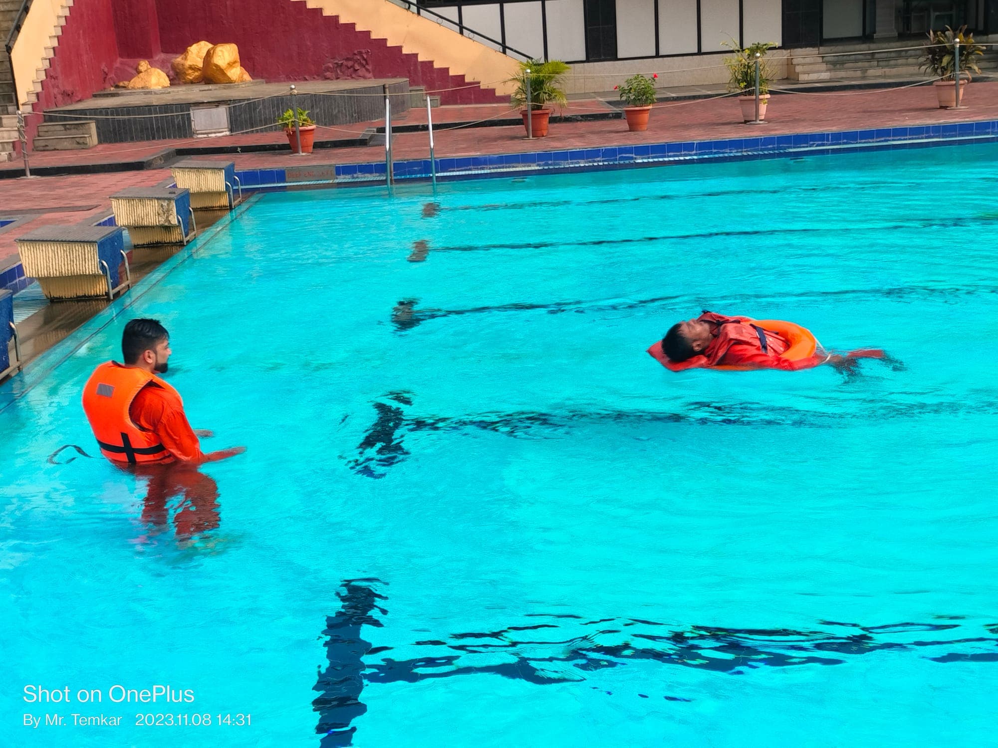 Participant floating on their back in a lifejacket in a training pool while a second participant observes from the water during sea survival training