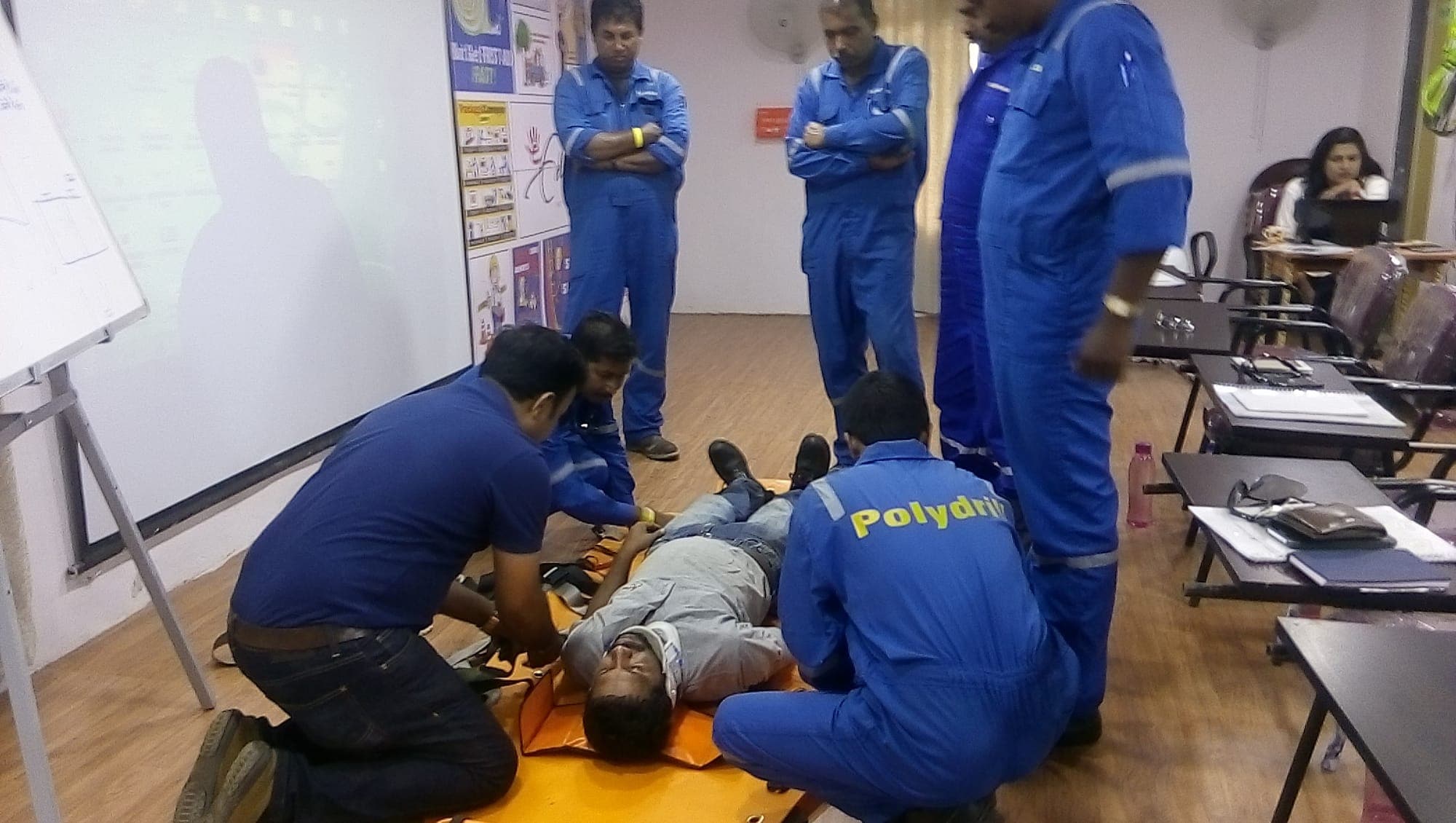 Participants kneeling to position a simulated casualty on a basket stretcher