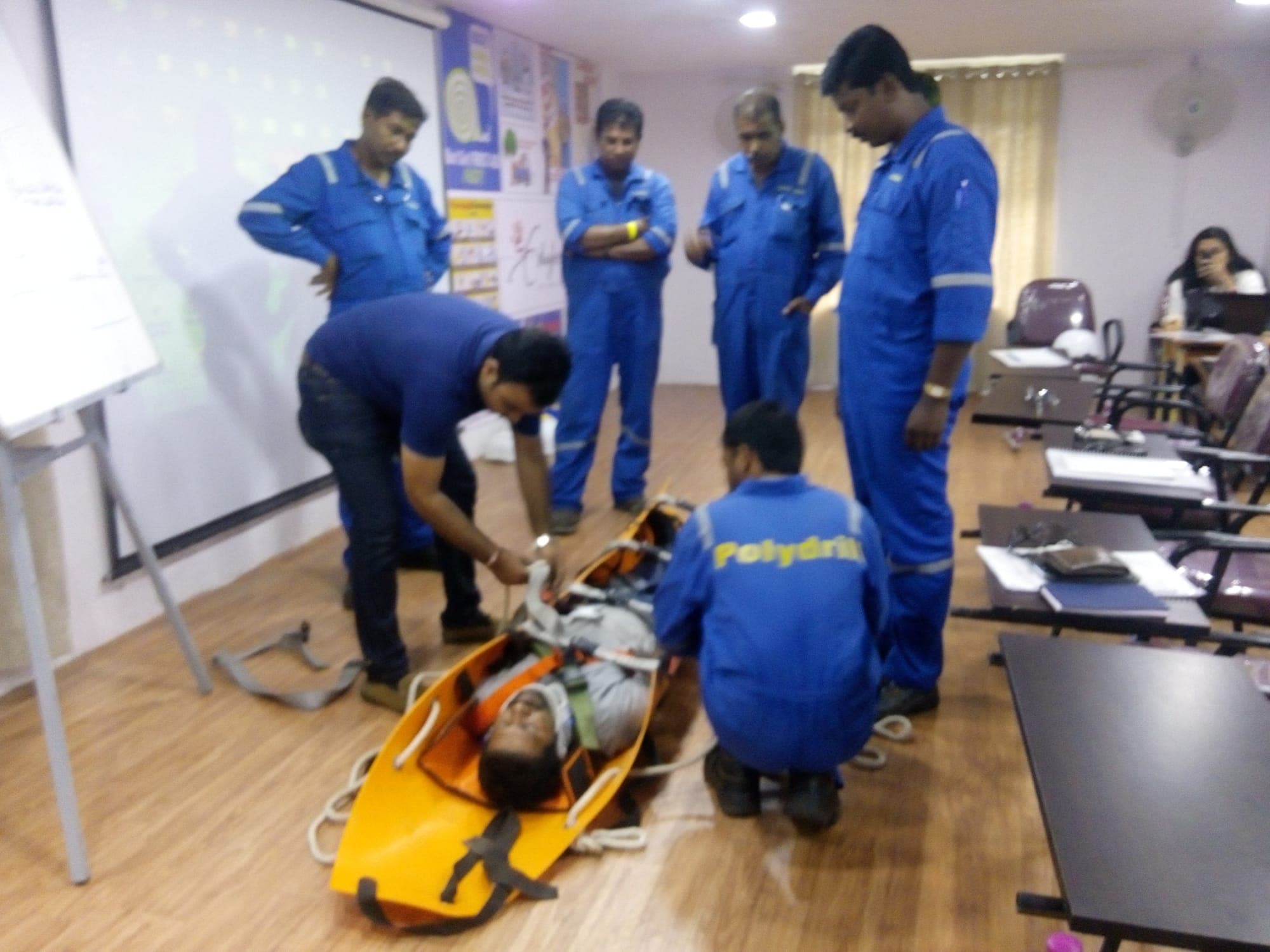 Group of participants practising stretcher handling around a casualty on the classroom floor