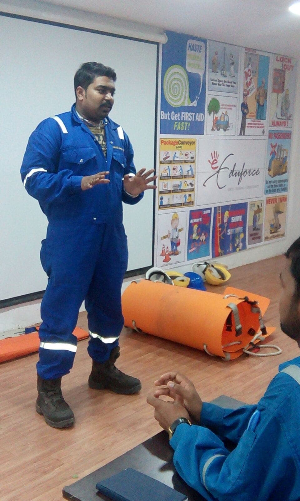 Trainer in coveralls demonstrating rescue equipment to seated participants