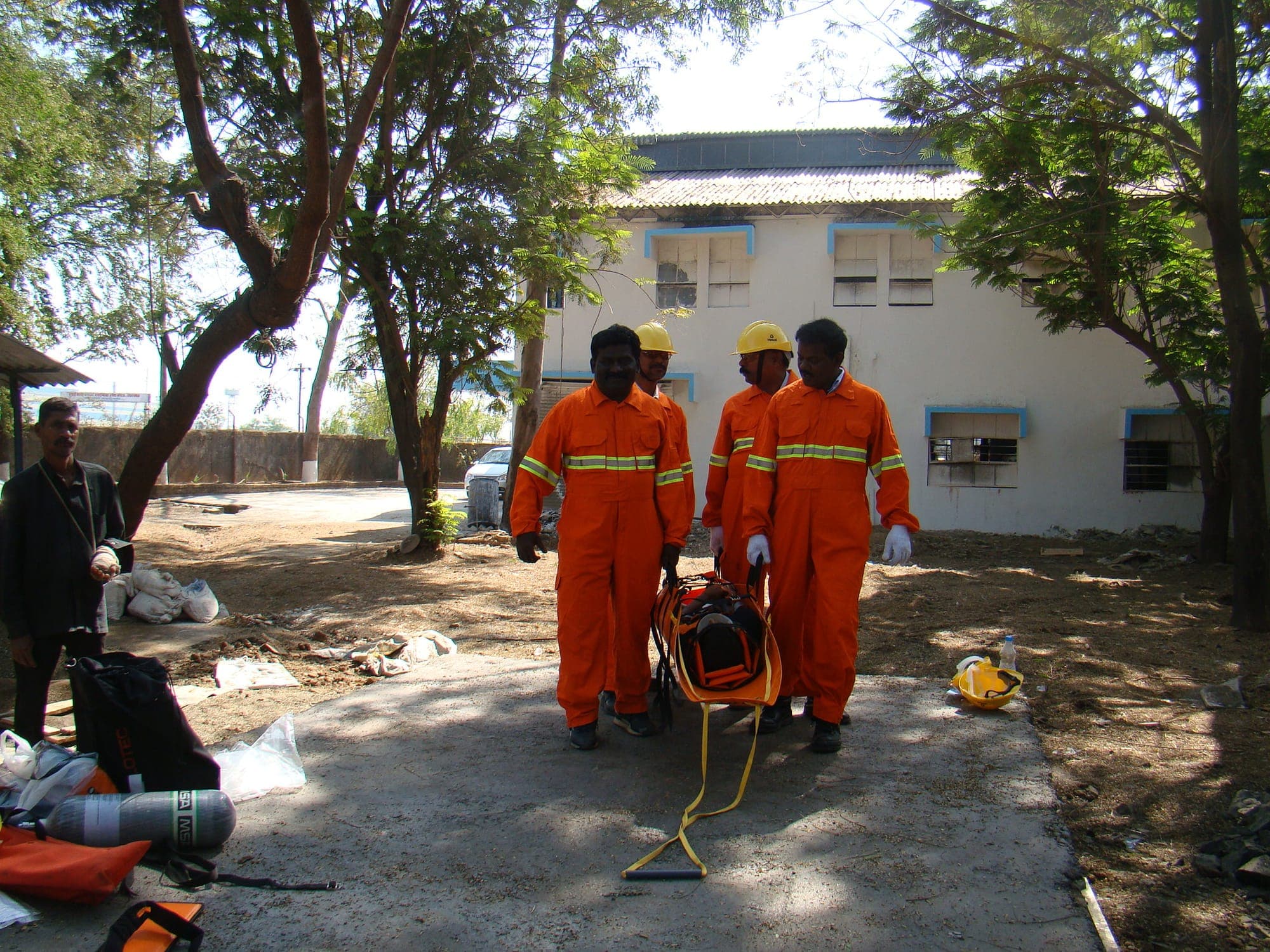Training team in orange coveralls carrying rescue equipment towards an outdoor practical training area