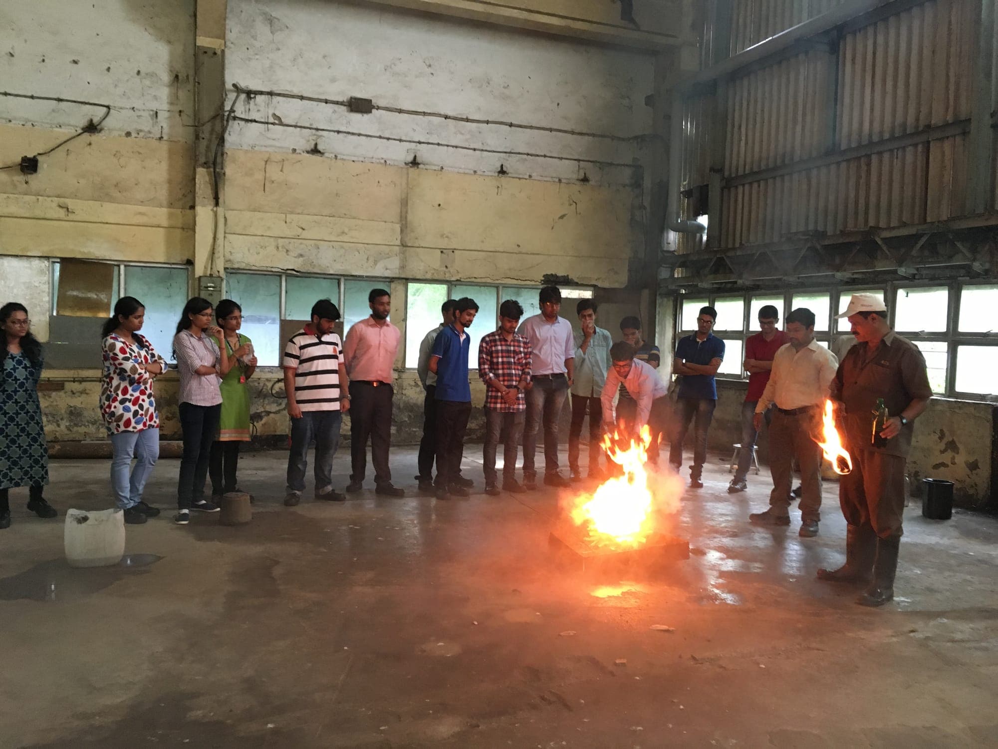 Instructor conducting a controlled fire demonstration indoors while a group of trainees observes
