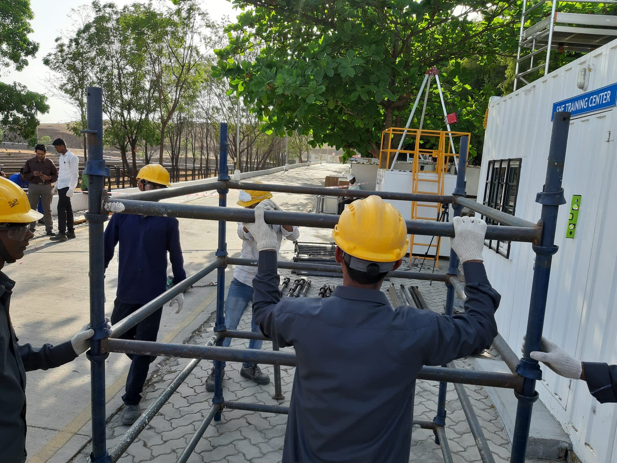 Participants in hard hats and gloves lifting and positioning the ledgers of a scaffold bay during a practical erection exercise