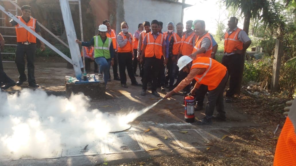 Participant discharging a fire extinguisher onto a training fire tray while a group observes
