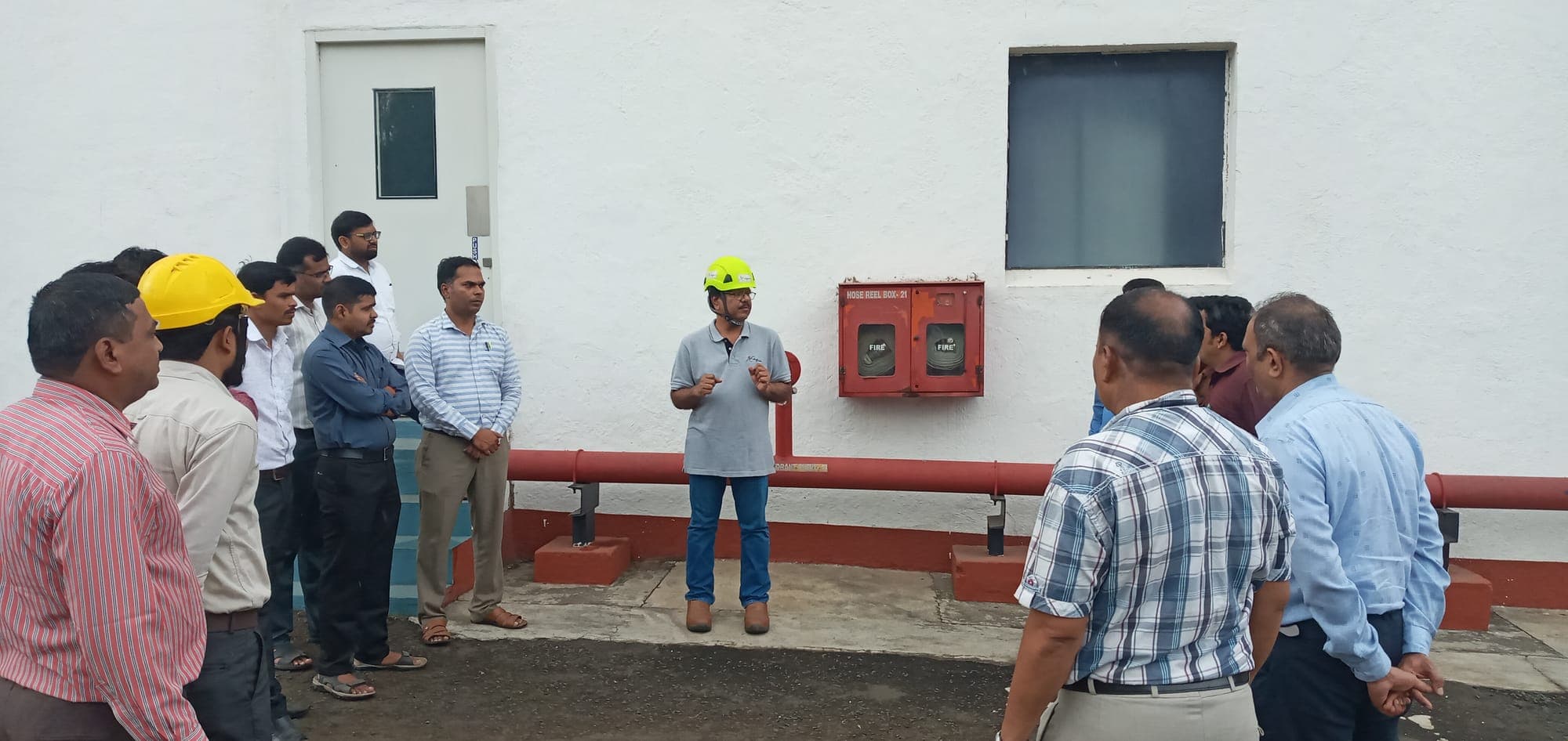 Instructor briefing a group at a wall-mounted fire hose reel cabinet during fire safety training