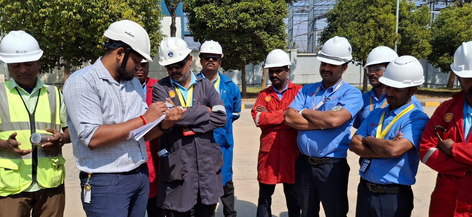 Trainer with a checklist briefing a group of participants in helmets beside a scaffold