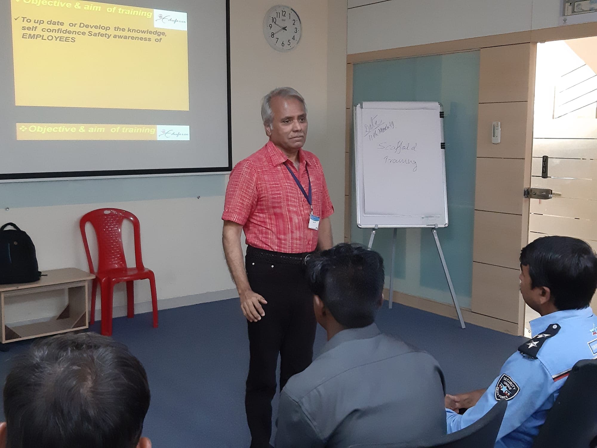 Trainer presenting the classroom part of a scaffold training course beside a projected slide and a flip chart headed Scaffold Training