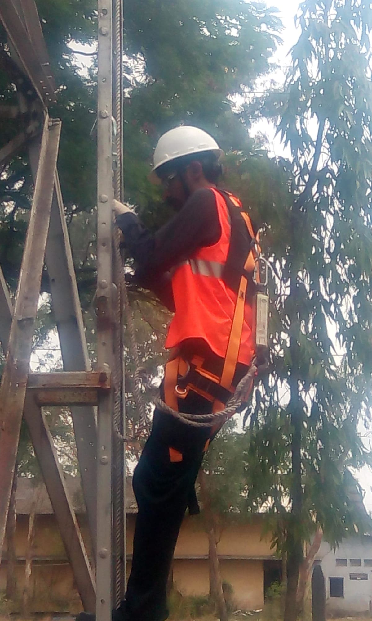 Trainee in a full body harness climbing a steel lattice structure with a fall arrest lanyard attached