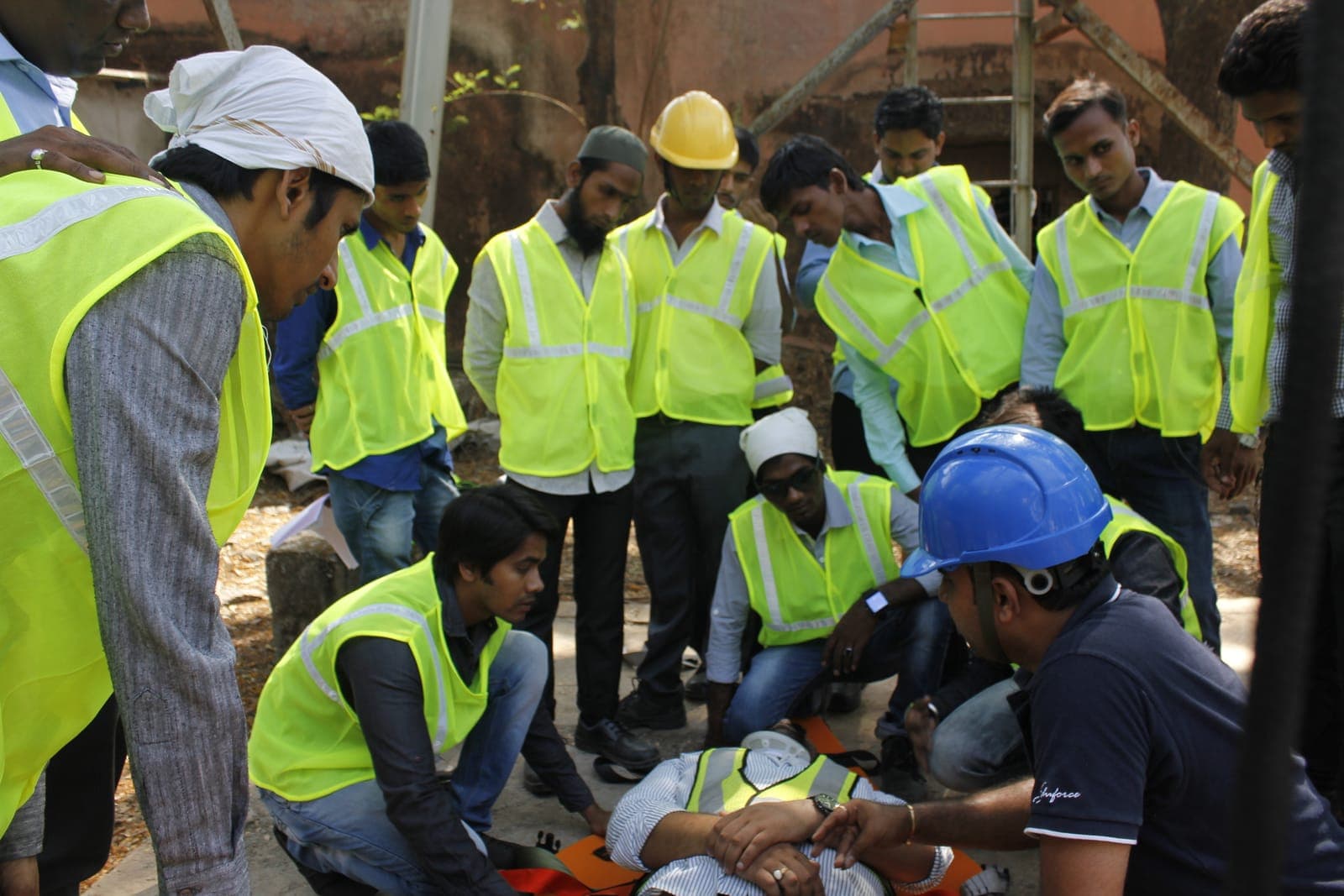 Trainees in high-visibility vests gathered round a casualty during a first aid practical, guided by an Eduforce trainer in a hard hat
