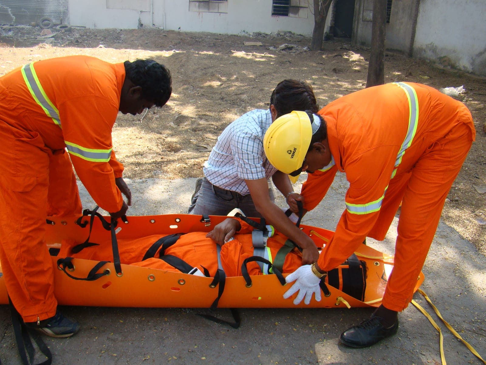 Rescue team in coveralls, gloves and a hard hat packaging a casualty into a rescue stretcher
