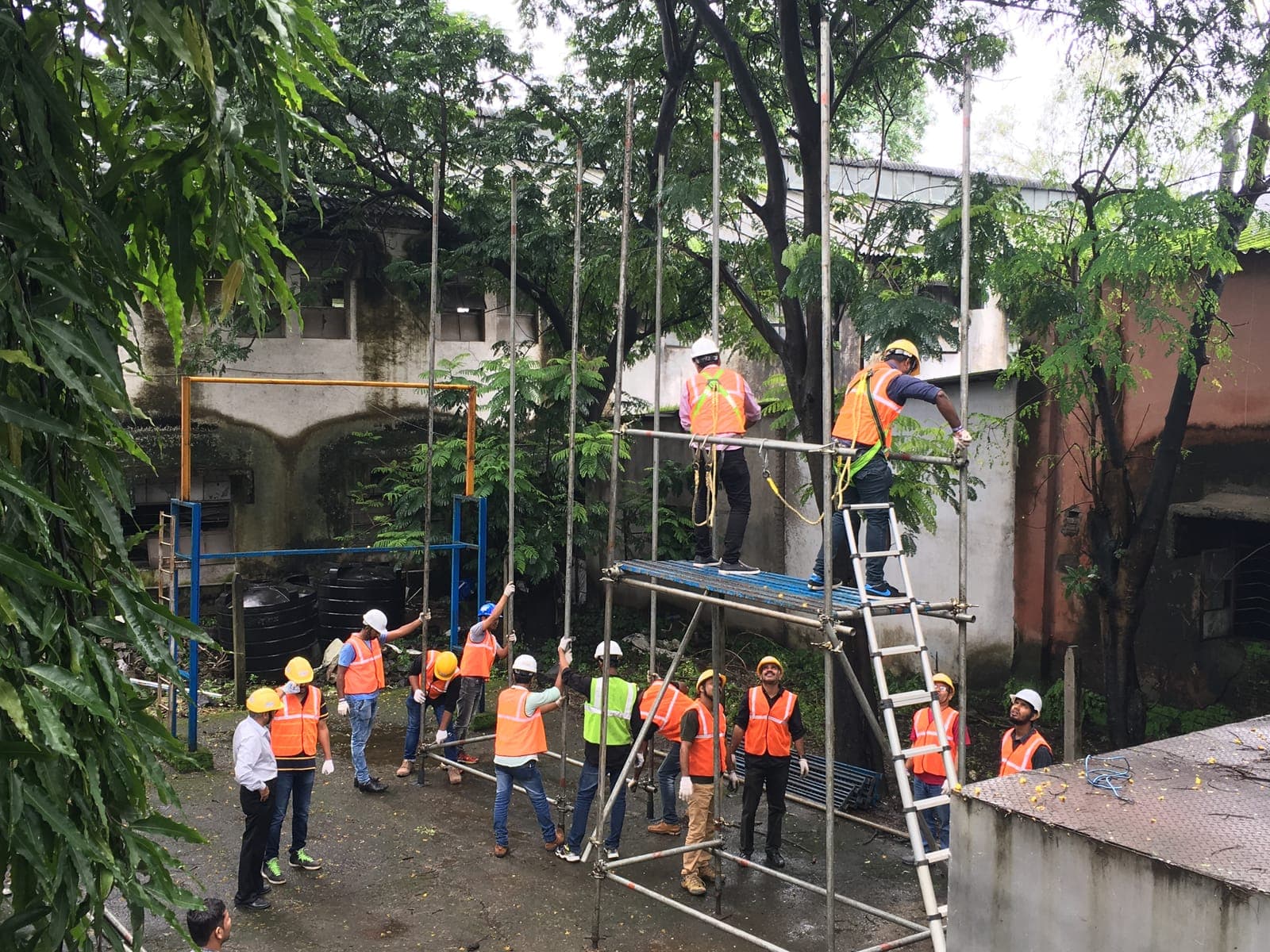 Trainees in hard hats and harnesses erecting a tall tube-and-fitting scaffold on site