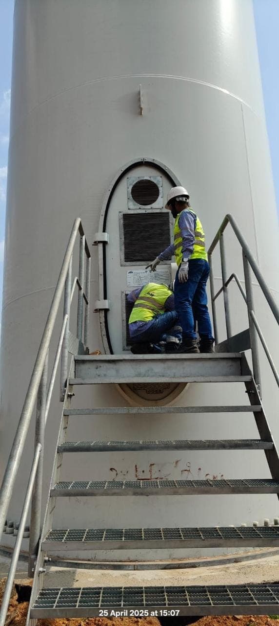 Two technicians in helmets and high-visibility vests at the entrance door of a wind turbine tower, above steel steps